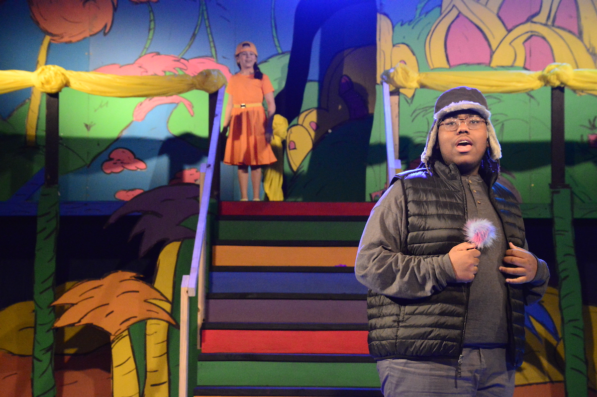 Academy student Jude holds a flower while singing on stage in Seussical